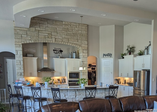 kitchen featuring white cabinets, a breakfast bar, wall chimney range hood, and stainless steel appliances