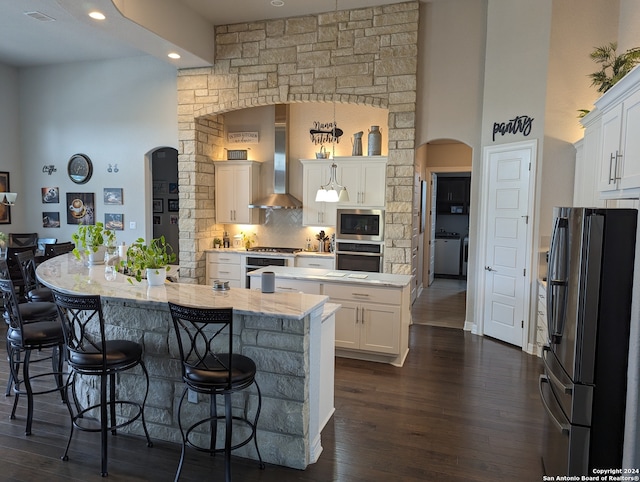 kitchen featuring wall chimney exhaust hood, white cabinetry, stainless steel appliances, tasteful backsplash, and a center island with sink