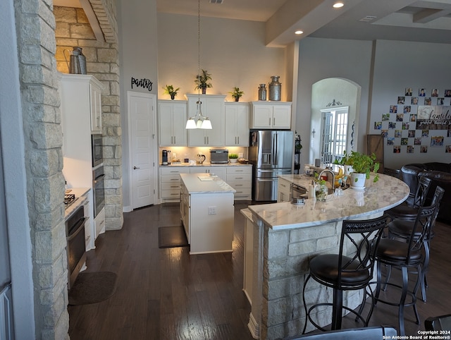 kitchen with white cabinetry, stainless steel appliances, a kitchen island with sink, a towering ceiling, and pendant lighting