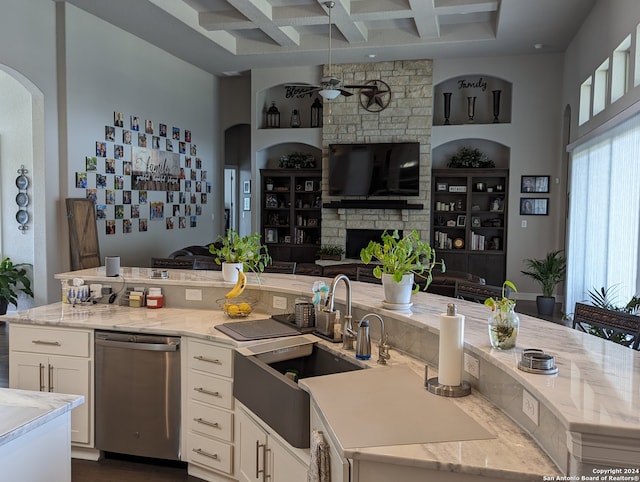 kitchen with stainless steel dishwasher, beam ceiling, a large fireplace, coffered ceiling, and light stone counters