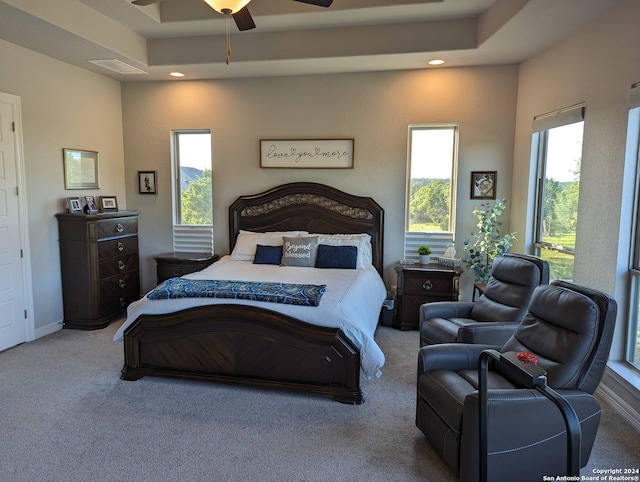 carpeted bedroom with ceiling fan and a tray ceiling