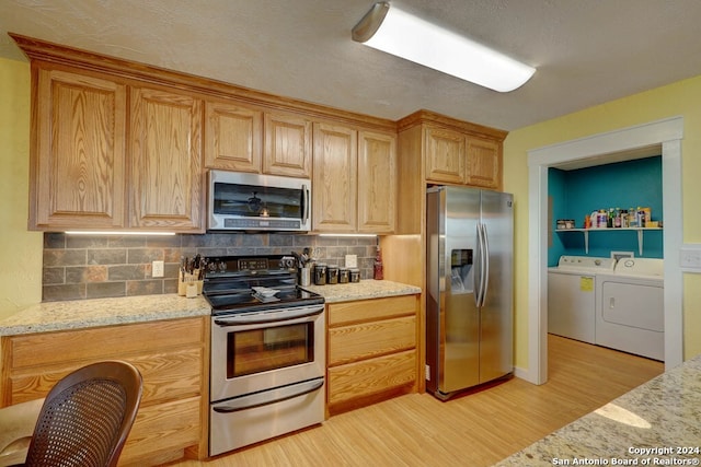 kitchen featuring light hardwood / wood-style flooring, tasteful backsplash, stainless steel appliances, washer and dryer, and light stone counters