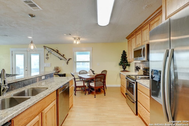 kitchen with light stone countertops, light hardwood / wood-style flooring, pendant lighting, sink, and appliances with stainless steel finishes