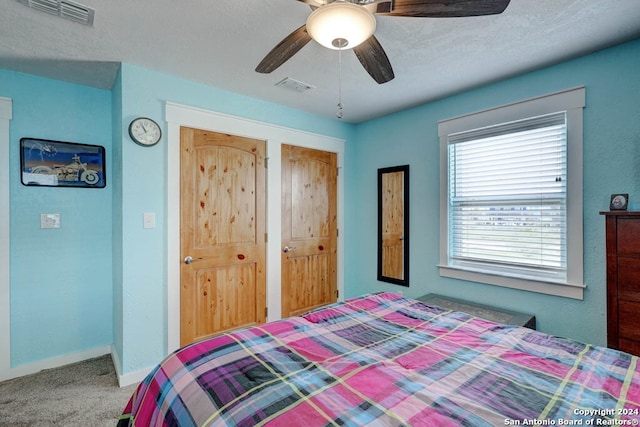 carpeted bedroom with a textured ceiling, two closets, and ceiling fan