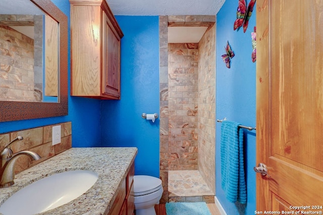 bathroom with tiled shower, a textured ceiling, tile flooring, oversized vanity, and toilet