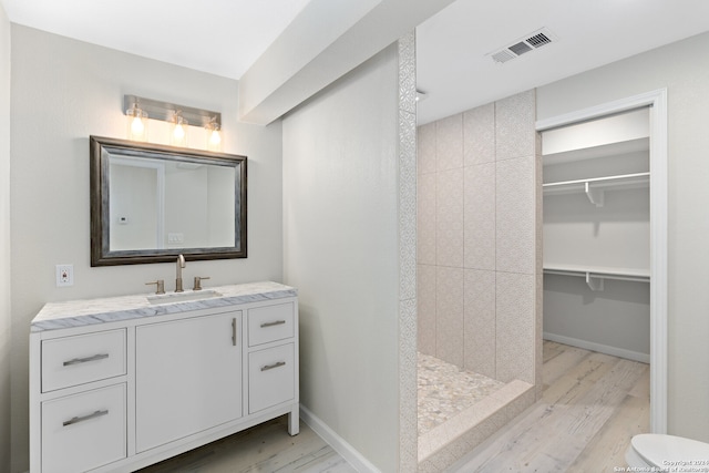 bathroom with a tile shower, hardwood / wood-style flooring, toilet, and oversized vanity