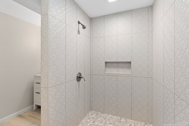 bathroom with wood-type flooring, a tile shower, and vanity