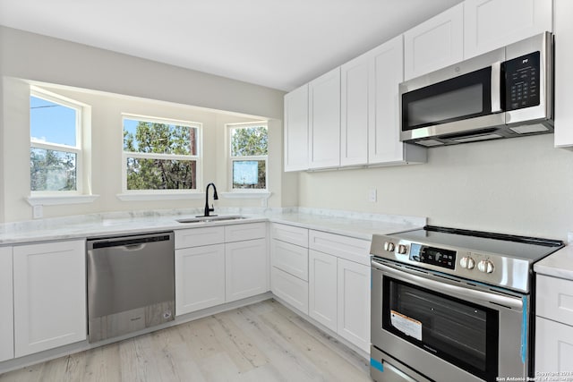 kitchen featuring light hardwood / wood-style flooring, stainless steel appliances, white cabinetry, light stone countertops, and sink