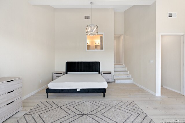 bedroom featuring a towering ceiling, light wood-type flooring, and an inviting chandelier