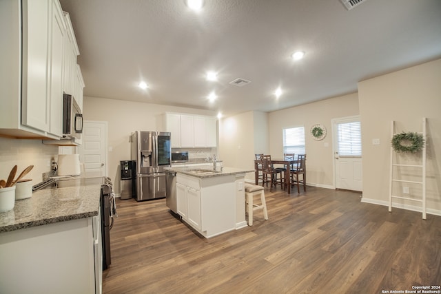 kitchen with stainless steel appliances, dark wood-type flooring, a center island with sink, and light stone countertops