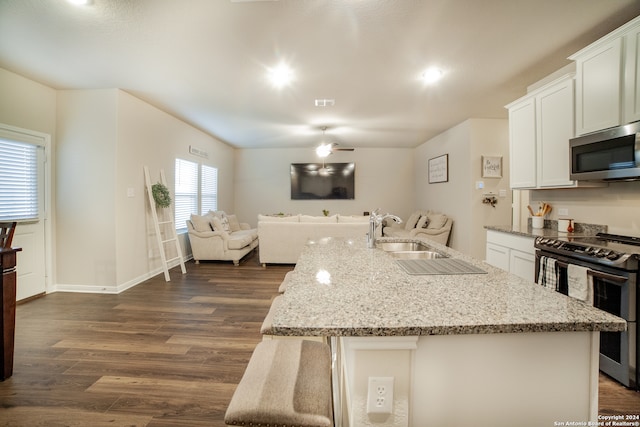 kitchen with light stone counters, dark hardwood / wood-style floors, stainless steel appliances, white cabinetry, and an island with sink