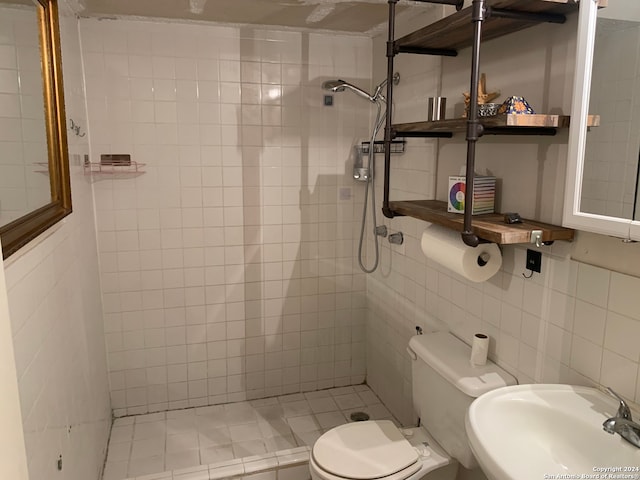 bathroom with tiled shower, sink, toilet, and tile walls