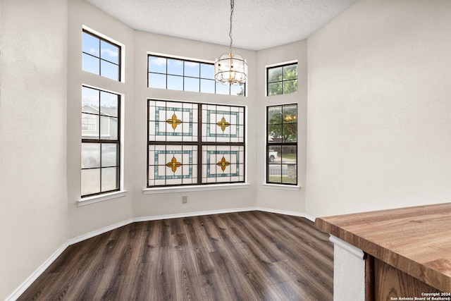 unfurnished dining area featuring dark hardwood / wood-style flooring, a textured ceiling, and an inviting chandelier