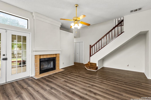 unfurnished living room with french doors, dark hardwood / wood-style floors, ceiling fan, a textured ceiling, and a tiled fireplace