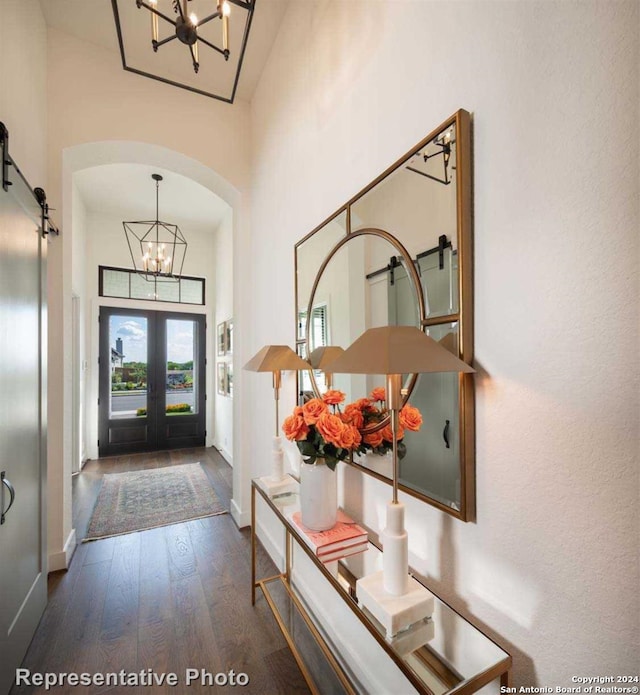 foyer entrance with french doors, a towering ceiling, a barn door, an inviting chandelier, and dark hardwood / wood-style floors