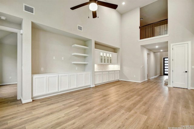 unfurnished living room featuring ceiling fan, a high ceiling, and light hardwood / wood-style flooring