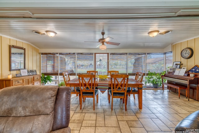 dining room with ceiling fan, wood walls, crown molding, and a wealth of natural light