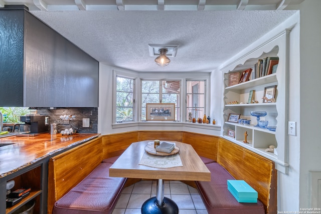 kitchen featuring a textured ceiling, breakfast area, light tile patterned floors, and backsplash