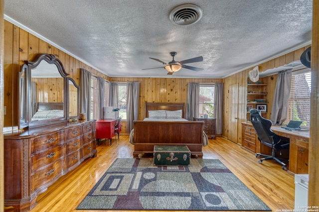 bedroom featuring a textured ceiling, light hardwood / wood-style floors, and wood walls