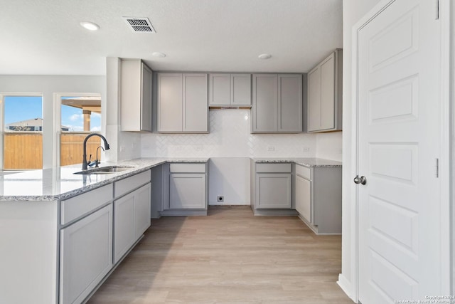 kitchen featuring sink, tasteful backsplash, light stone counters, gray cabinets, and light wood-type flooring