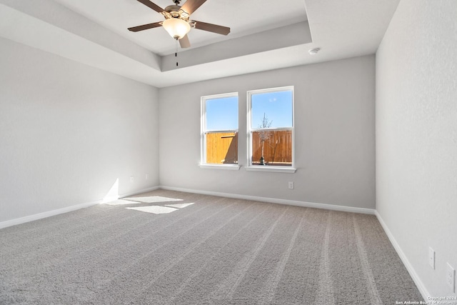 carpeted empty room with a raised ceiling and ceiling fan