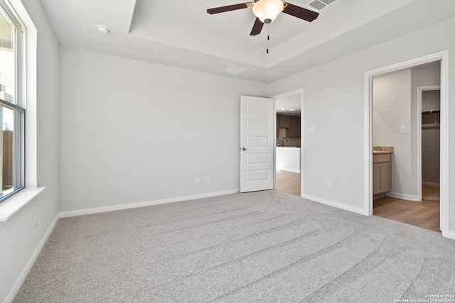 unfurnished bedroom with light carpet, a raised ceiling, ceiling fan, a spacious closet, and a closet