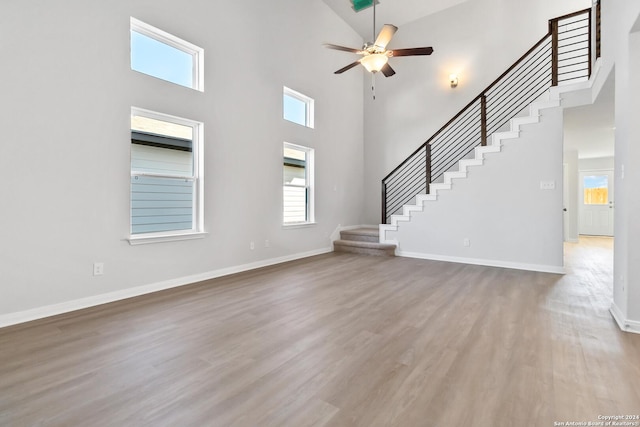 unfurnished living room featuring ceiling fan, wood-type flooring, and a high ceiling