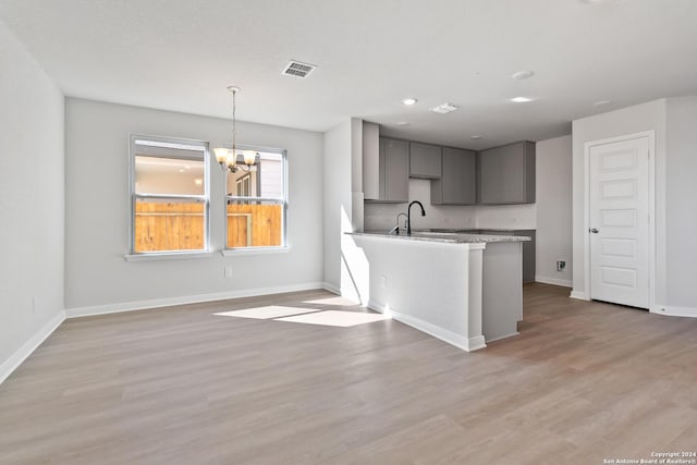 kitchen featuring gray cabinetry, backsplash, light hardwood / wood-style flooring, decorative light fixtures, and a chandelier