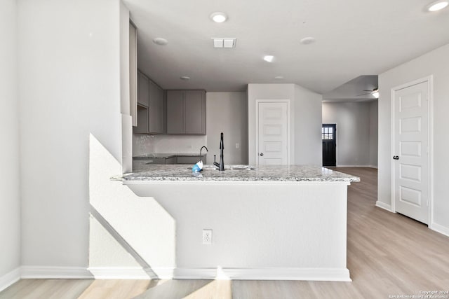 kitchen featuring kitchen peninsula, light stone countertops, gray cabinetry, sink, and light hardwood / wood-style flooring