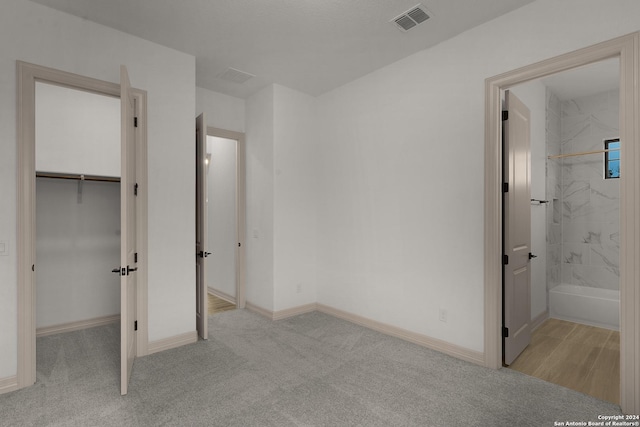 unfurnished bedroom with a walk in closet, light carpet, connected bathroom, and a closet