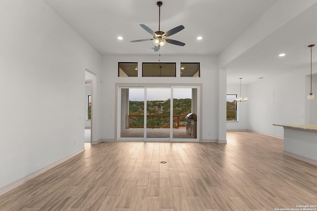 unfurnished living room with ceiling fan with notable chandelier and light hardwood / wood-style flooring