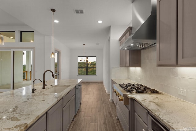 kitchen with sink, wall chimney exhaust hood, hanging light fixtures, light stone counters, and appliances with stainless steel finishes