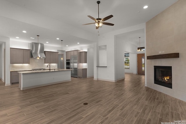 kitchen with a tile fireplace, wall chimney exhaust hood, dark hardwood / wood-style floors, an island with sink, and decorative light fixtures