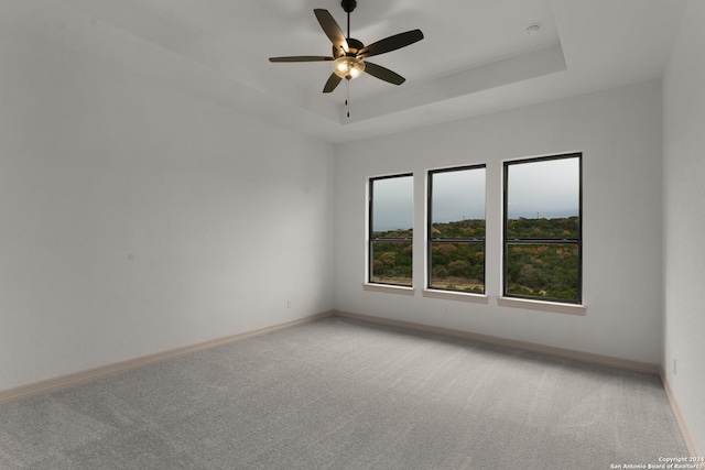 carpeted empty room with a raised ceiling and ceiling fan