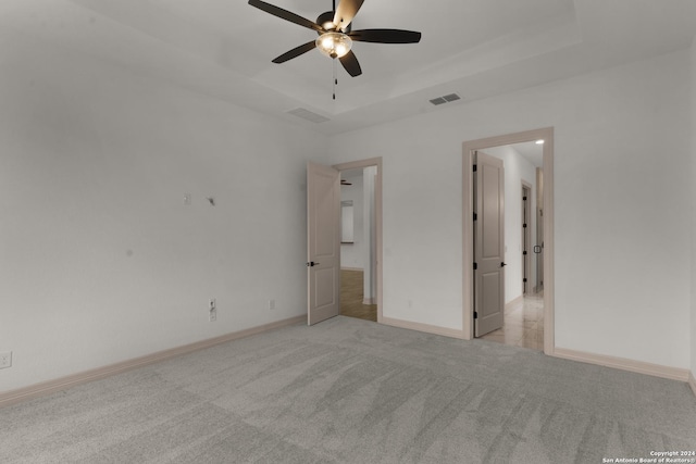 spare room with a raised ceiling, ceiling fan, and light colored carpet