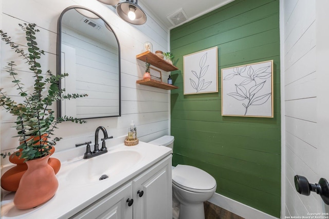 half bathroom with toilet, vanity, visible vents, and wooden walls