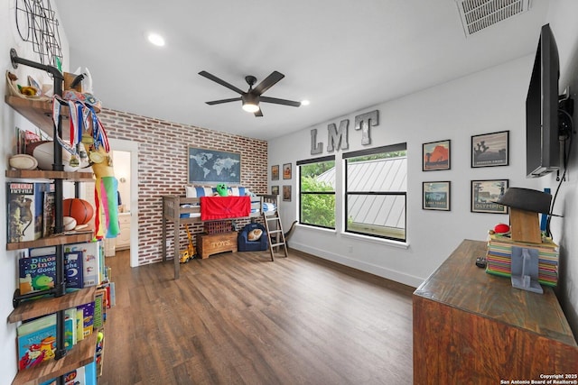 interior space featuring baseboards, visible vents, a ceiling fan, brick wall, and wood finished floors