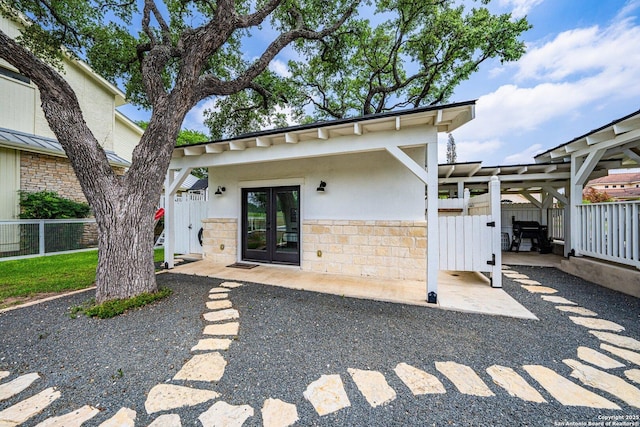 entrance to property featuring stone siding, fence, french doors, a patio area, and stucco siding