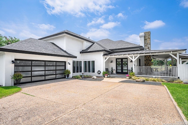 view of front of property featuring driveway, roof with shingles, an attached garage, covered porch, and french doors