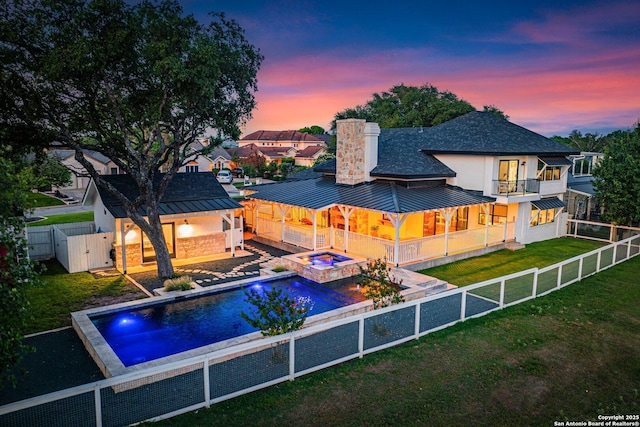 back of property featuring a standing seam roof, a fenced backyard, a lawn, and a balcony