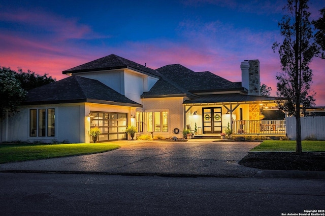 view of front of home featuring driveway, a garage, a chimney, covered porch, and french doors