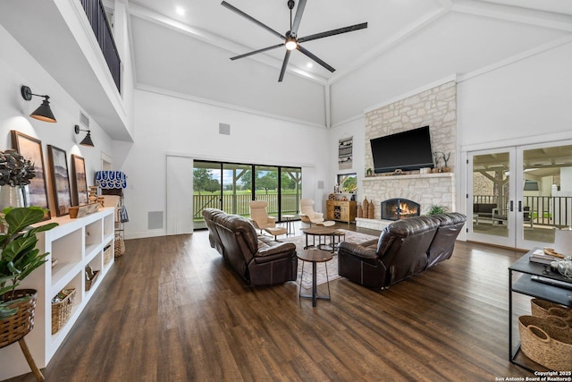 living area with ceiling fan, high vaulted ceiling, a stone fireplace, wood finished floors, and french doors