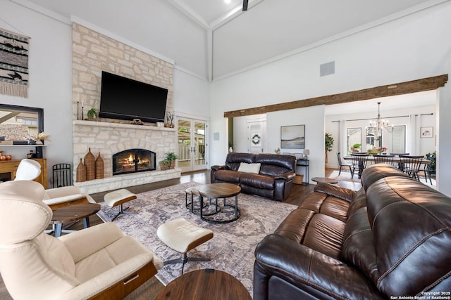 living area with a chandelier, a stone fireplace, wood finished floors, a towering ceiling, and visible vents