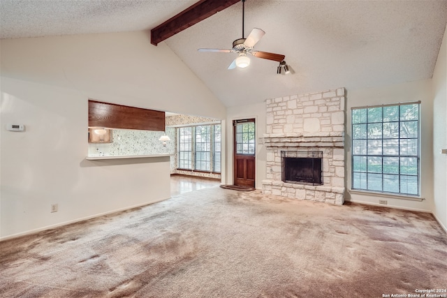 unfurnished living room with beam ceiling, carpet floors, a stone fireplace, and a wealth of natural light