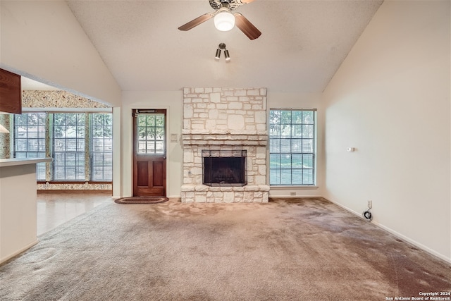 unfurnished living room featuring plenty of natural light, ceiling fan, a stone fireplace, and carpet floors