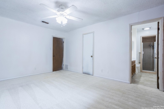 unfurnished bedroom featuring ensuite bath, ceiling fan, a textured ceiling, light carpet, and a closet