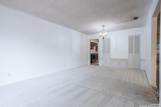 unfurnished room featuring a textured ceiling, light colored carpet, and a notable chandelier