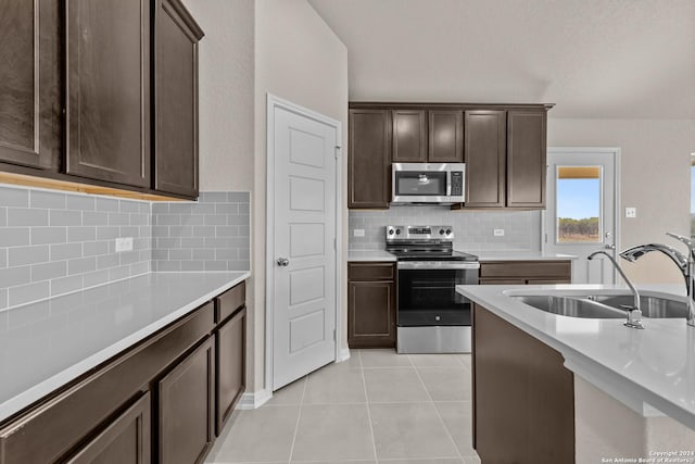 kitchen with backsplash, sink, light tile patterned floors, dark brown cabinets, and stainless steel appliances