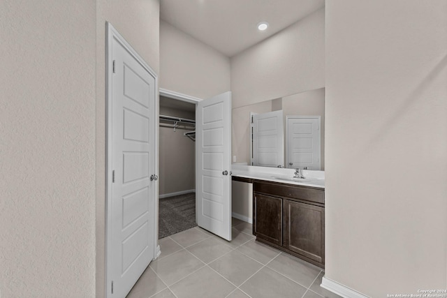 full bathroom with tile patterned floors, vanity, a walk in closet, and baseboards