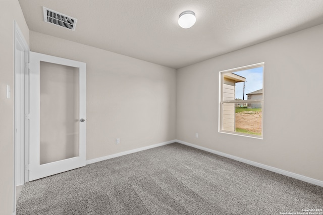 carpeted empty room featuring visible vents, a textured ceiling, and baseboards
